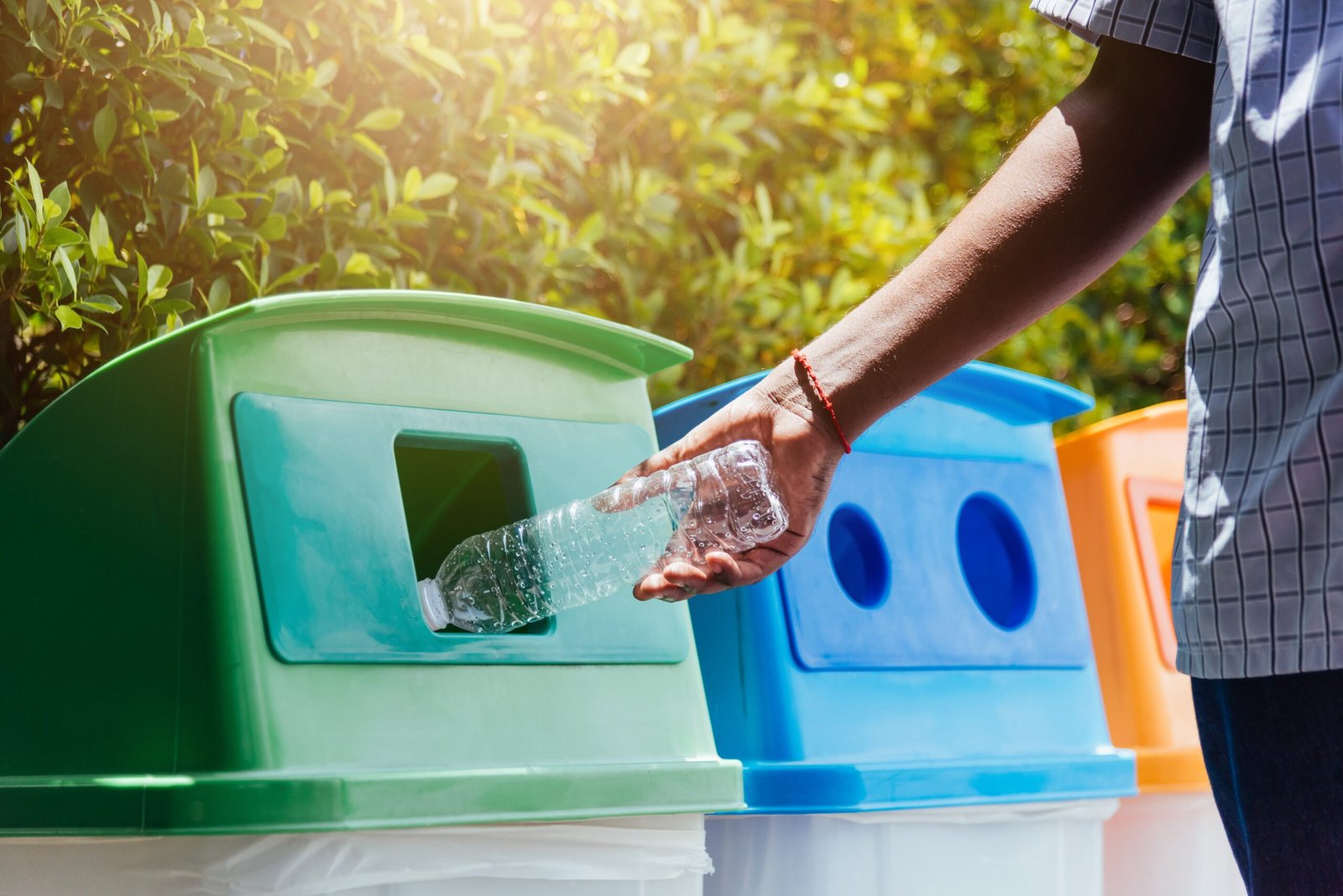hand throwing an empty plastic water bottle in the recycling garbage trash scaled